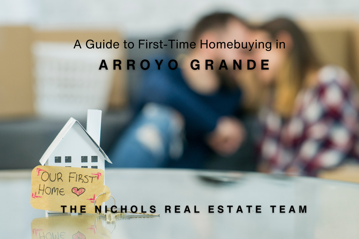 A small model house with a key and a handwritten tag that reads "Our First Home ❤️" sits on a reflective surface. In the blurred background, a Arroyo Grande First-Time Homebuyers couple is sitting together. Overlay text reads, "A Guide to First-Time Homebuying in Arroyo Grande," with The Nichols Real Estate Team branding.
